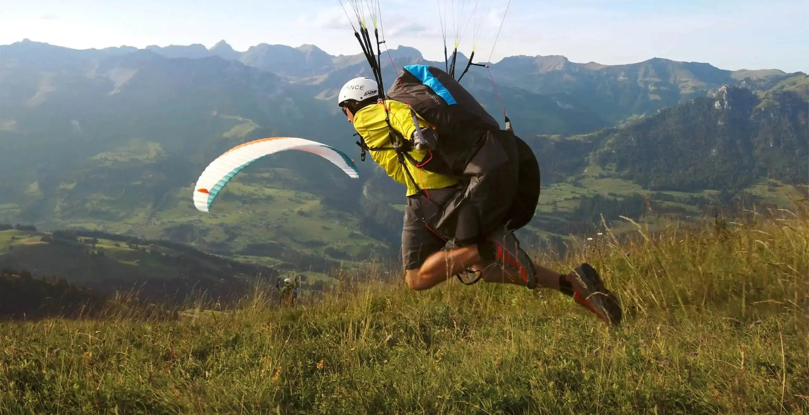 Startvorbereitung für startender Gleitschirmflieger an einem Startplatz in den Bergen mit grünen saftigen Wiesen.