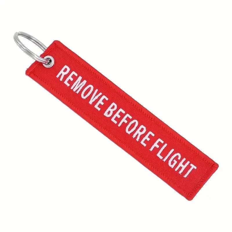 Schlüsselanhänger Remove before Flight für Gleitschirmpiloten, rot mit weißem Text, doppelseitig gewebt, ideal für Gurtzeug oder Schlüssel.
