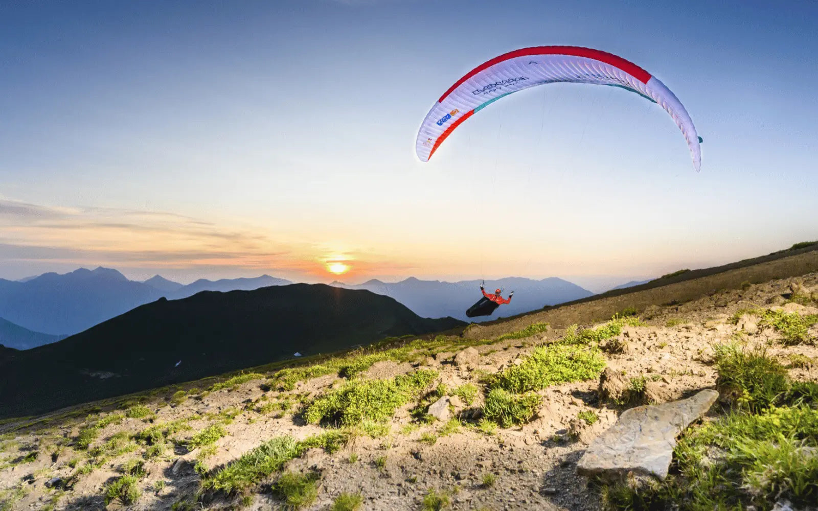 FAQ zum thema gleitschirmfliegen. paraglider gleitet knapp über einem Bergkamm entlang in Abenddämmerung und Sonnenuntergang.