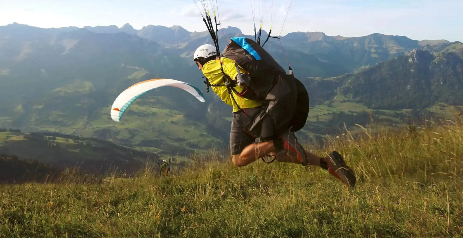 Startvorbereitung für startender Gleitschirmflieger an einem Startplatz in den Bergen mit grünen saftigen Wiesen.