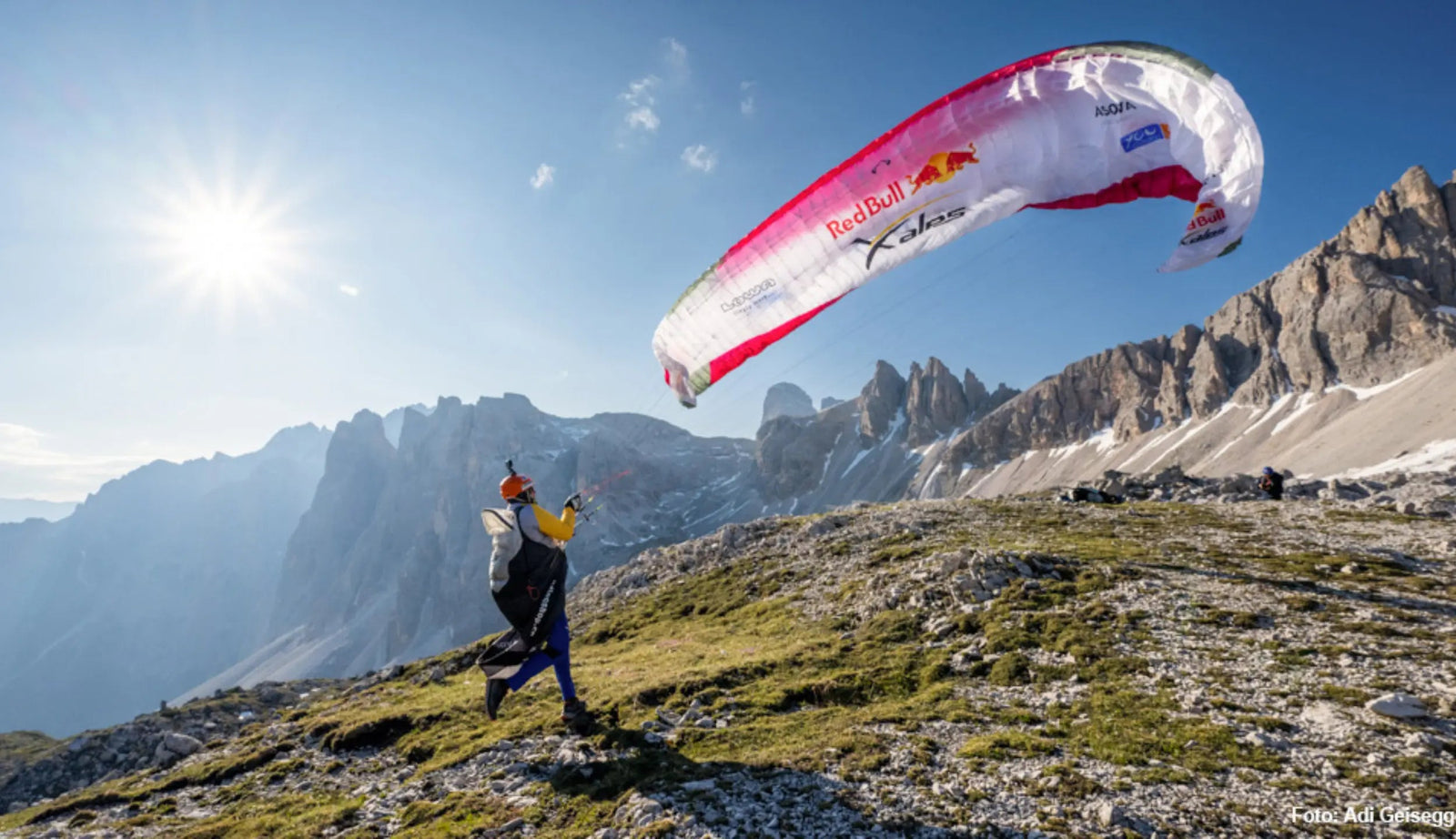 Chrigel Maurer am X-Alps Wettrennen rückwärts startend auf einem Berg bei strahlendem Sonnenschein