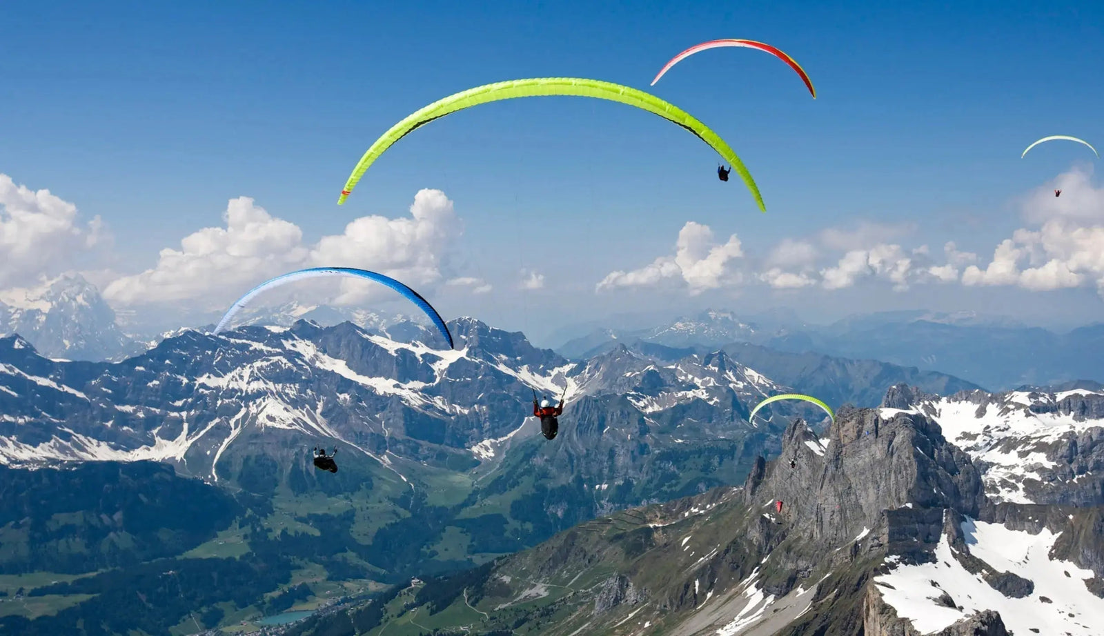 Sehr viele Gleitschirme fliegen in bewegter Luft und schöner Aussicht über Berge und Flachland für Blogartikel zum Thema Gleitschirmklassen