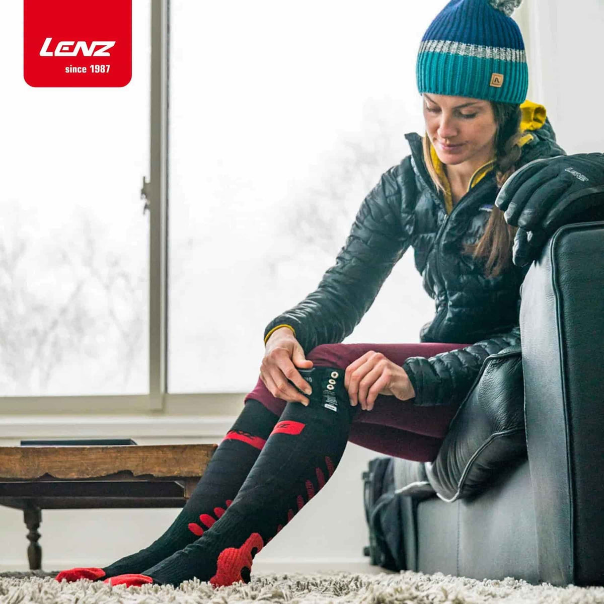 Frau auf Couch mit Lenz HEAT SOCK 5.1 Toe Cap Regular Fit, ideal für Winteraktivitäten, zeigt Passform und Komfort dieser beheizten Funktionssocken mit integriertem Schienbeinprotektor.