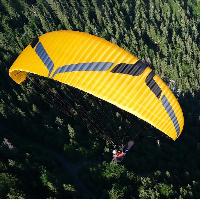 Ozone Swift 6 (High EN-B) Gleitschirm beim Paragliding über einem Wald, ideal für erfahrene Piloten, bekannt für Agilität und Leistung.