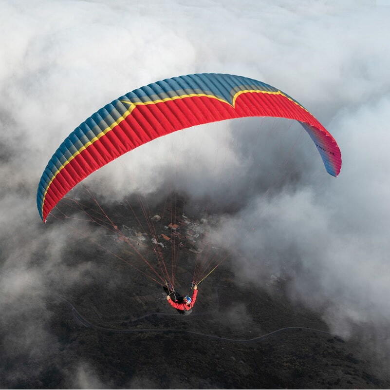 Ein Gleitschirmflieger mit einem Ozone Rush 6 (High EN-B) Schirm, der für hohe Leistung und Sicherheit beim Paragliding in der Luft sorgt.