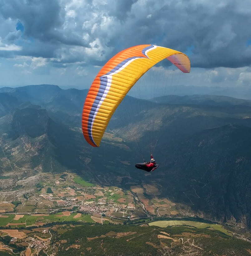 Ein Gleitschirmflieger mit einem Ozone Rush 6 (High EN-B) Schirm, der für hohe Leistung und Sicherheit beim Paragliding in der Luft sorgt.