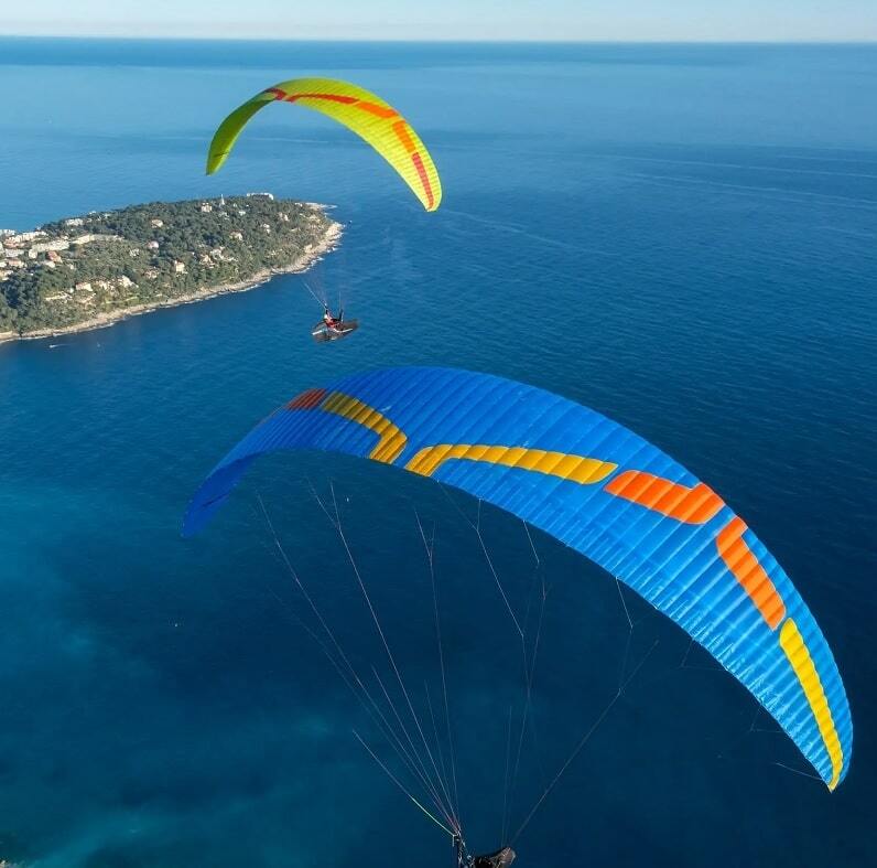 Zwei Paragleiter, darunter der Ozone Zeno 2 (EN-D), fliegen über das Wasser, zeigen seine beeindruckende Leistung und Stabilität für erfahrene XC-Piloten.