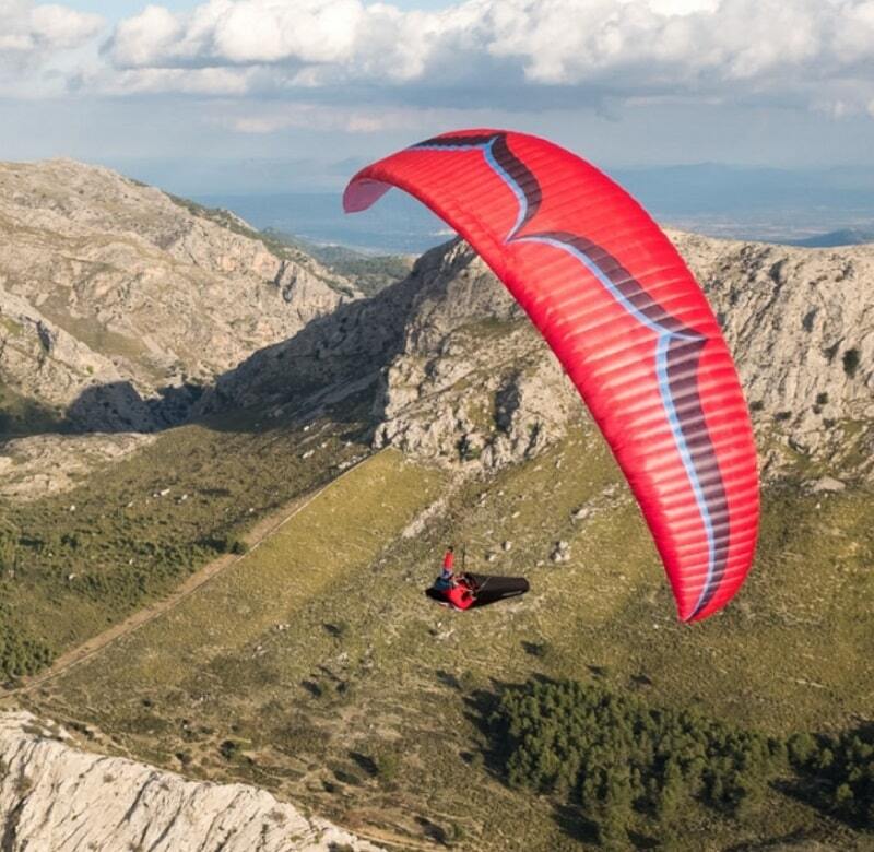 Person gleitet mit Ozone Alpina 4 (EN-C) Paraglider über Berglandschaft, repräsentiert leichtgewichtige Sportleistung und hohe Sicherheit. Perfekt für erfahrene Gleitschirmpiloten.