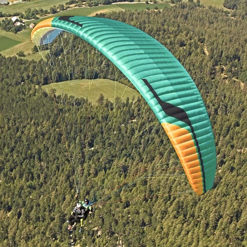 Niviuk Takoo 5 Tandemschirm schwebt über einem Wald, ideal für professionelle Doppelsitzerpiloten. Komfort und Stabilität für unvergessliche Flüge.