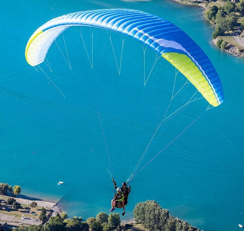 Niviuk Takoo 5 Tandemschirm im Flug über Wasser, ideal für professionelle Tandempiloten. Perfekte Balance aus Komfort und Stabilität für hochwertige Paragliding-Erlebnisse.