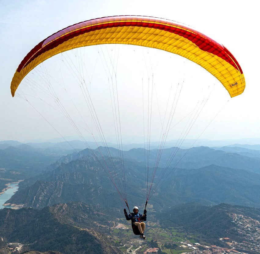 Person mit gelbem und rotem GIN Avid Gleitschirm über Berglandschaft, symbolisiert Abenteuer und präzises Handling für Streckenflieger. Ideal für XC-Abenteuer.