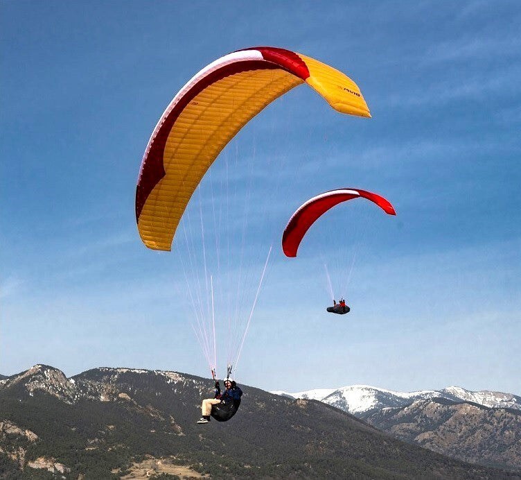 Person mit gelbem und rotem GIN Avid Gleitschirm über Berglandschaft, symbolisiert Abenteuer und präzises Handling für Streckenflieger. Ideal für XC-Abenteuer.