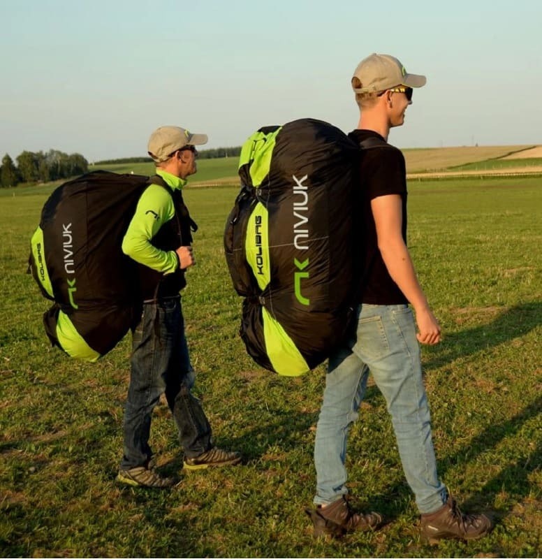 Zwei Männer tragen den Niviuk Koli Bag Schnellpacksack, ideal für Gleitschirmfliegen, mit bequemen Schultergurten und großer Öffnung für schnelles Packen.