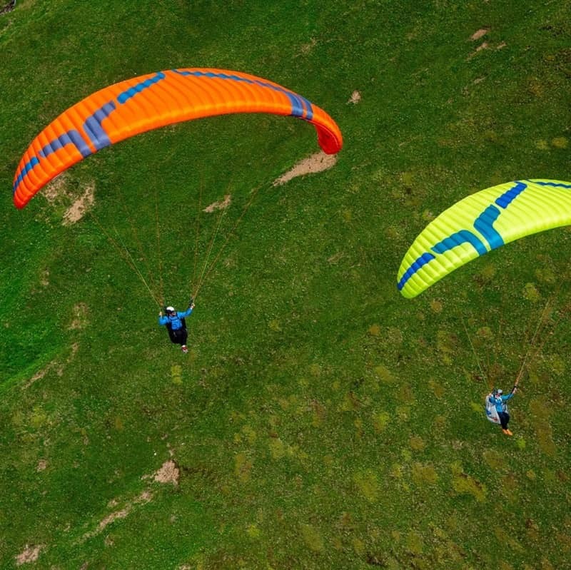 Ozone Buzz Z7 Gleitschirm beim Paragliding über einer Stadt, zeigt innovative Flügelform und verbesserte Stabilität, ideal für XC-Flüge mit hoher passiver Sicherheit.