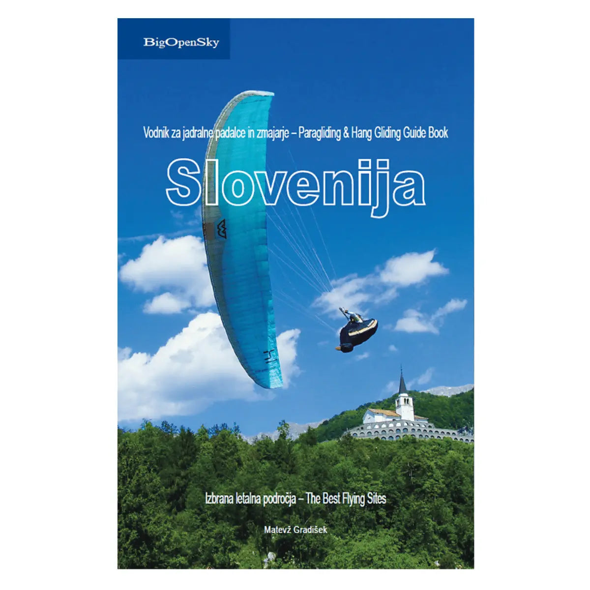 Fluggebietsführer Slovenija von BigOpenSky: Ein blauer Gleitschirm mit Pilot fliegt vor einer Bergkulisse mit einem Gebäude, detailliert in diesem Buch über die besten Fluggebiete.