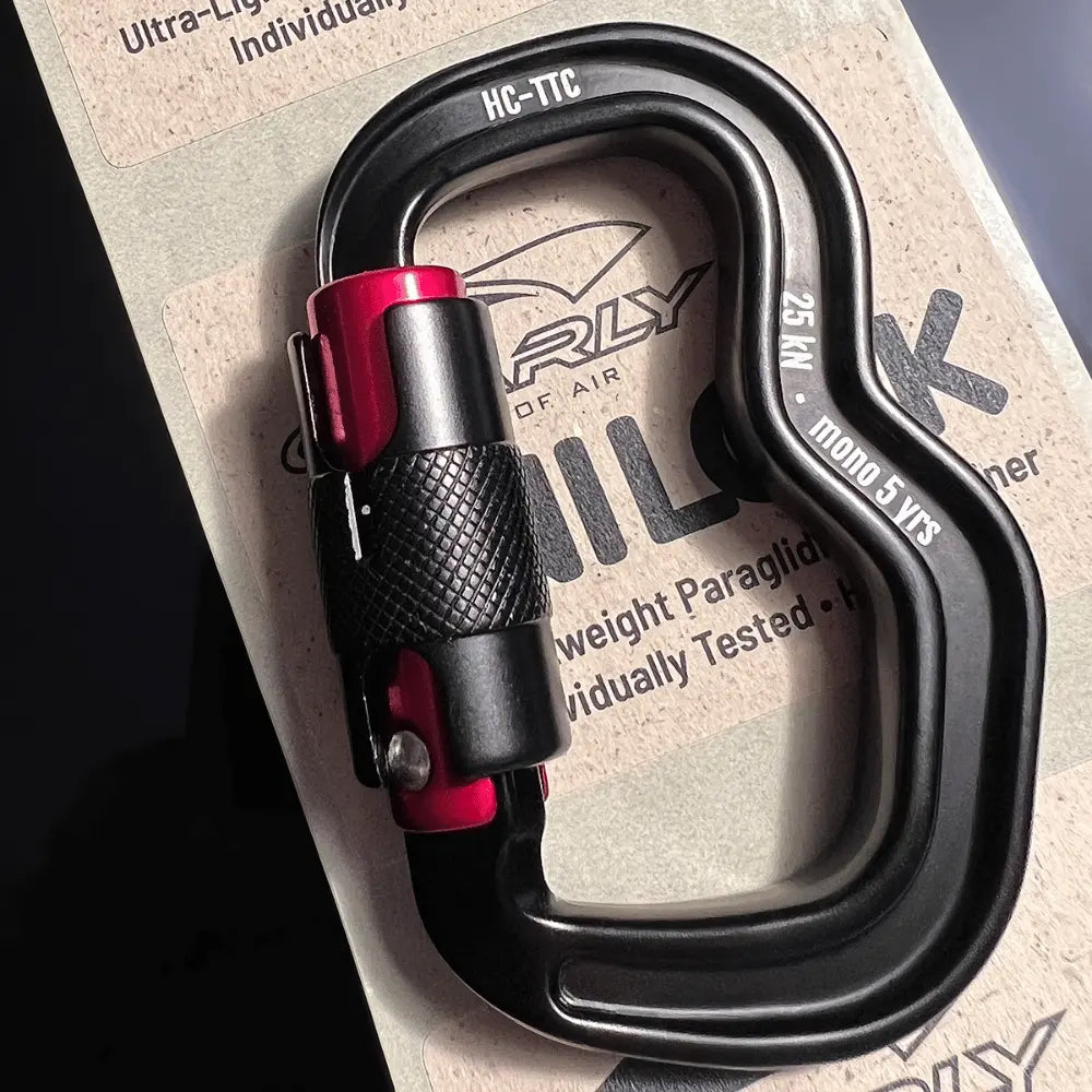 Finsterwalder Unilock Karabiner in roter Ausführung, ultraleicht, Nahaufnahme eines strapazierfähigen und sicheren Paragliding-Verbinders mit spezieller Schnapperöffnung für einfaches Einhängen liegend auf der Verpackung.