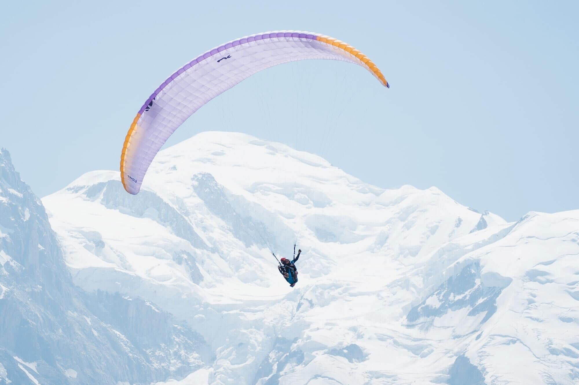 Paragliding24.ch - Physischer Gutschein, zeigt eine Person beim Paragliding über verschneiten Bergen. Perfektes Geschenk für Abenteuerliebhaber, bereitgestellt vom Schweizer Gleitschirmshop.