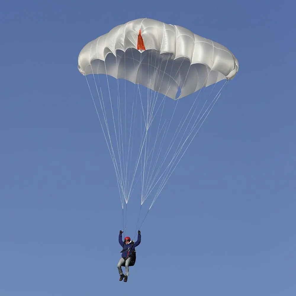 Charly TargetCross ST Light - Tandem Notschirm im Einsatz, zeigt eine Person in blauer Jacke mit steuerbarem, weißen Fallschirm und roter Flagge am Himmel.
