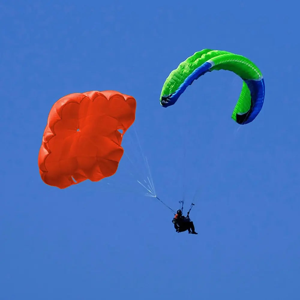 Person in Paragliding-Gurtzeug mit Niviuk Octagon 2 Rettungsschirm und Hauptschirm, beide entfaltet, im klaren Himmel, zeigt höchste Sicherheit und Stabilität in Notfällen.