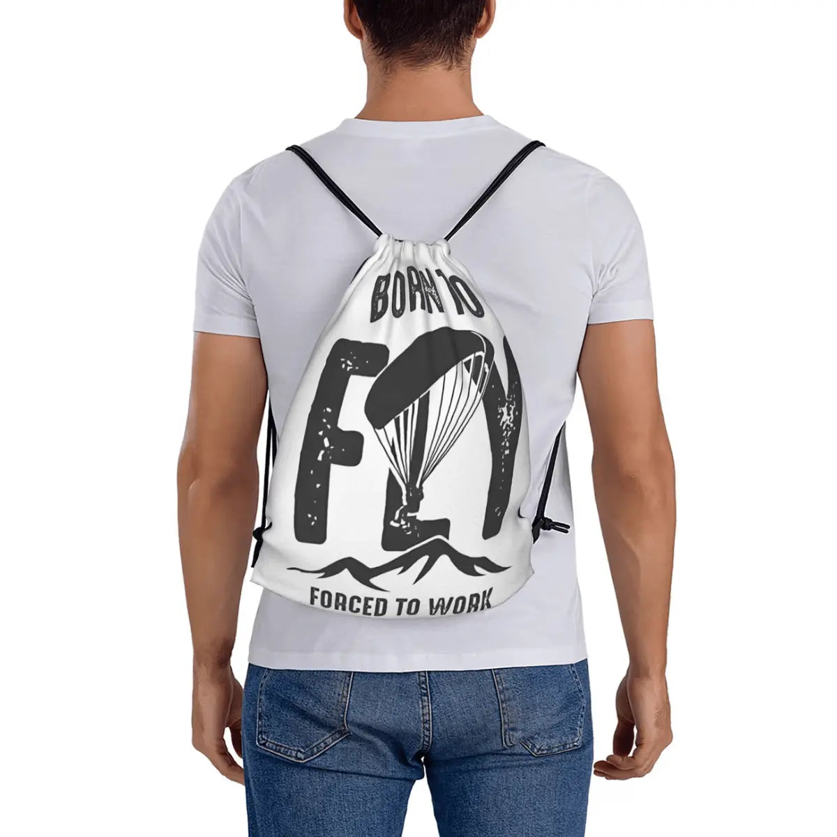 Sportbeutel mit der Aufschrift "Born to Fly" und einem Paragliding-Motiv, getragen von einer Person mit Jeans und weißem T-Shirt.