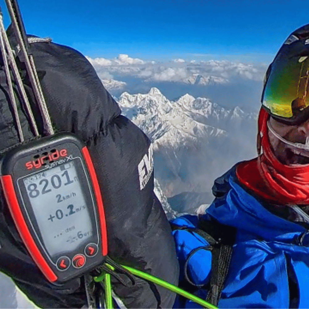 Person mit blauer Jacke und Schutzbrille hält das Syride SYS&#39;Nav XL, ein vielseitiges GPS-Variometer für Gleitschirmflieger, ideal für Abenteuer und Wettbewerbe.