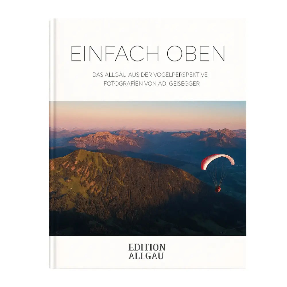 Hardcover-Fotobuch „Einfach Oben“ mit Luftaufnahme des Allgäus, Paraglider über Bergkamm bei Sonnenuntergang. Fotografien von Adi Geisegger, veröffentlicht von Edition Allgäu.
