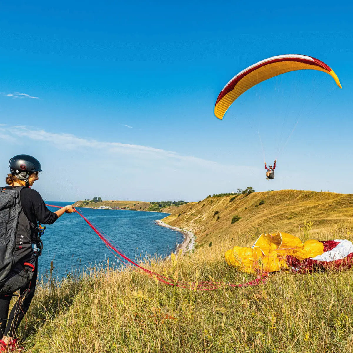 Person mit gelbem und rotem GIN Avid Gleitschirm über Berglandschaft, symbolisiert Abenteuer und präzises Handling für Streckenflieger. Ideal für XC-Abenteuer.