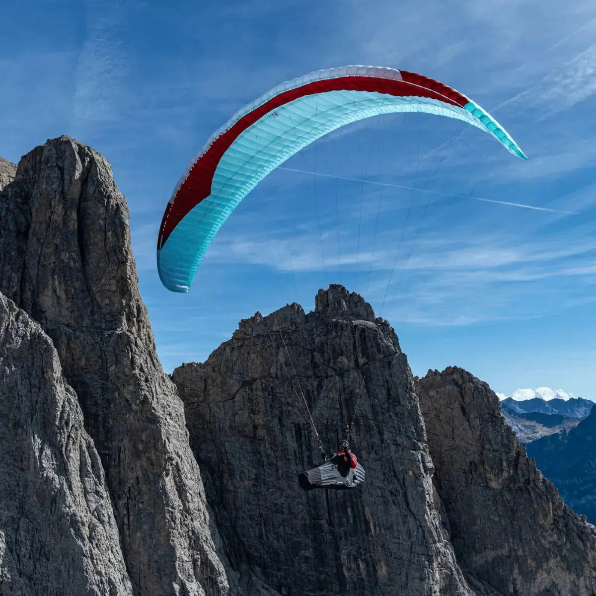 Pilot schwebt unter türkis-rotem Gin Bonanza 3 (EN-C) Gleitschirm vor felsigen Bergen, ideal für leistungsorientierte Streckenflüge.