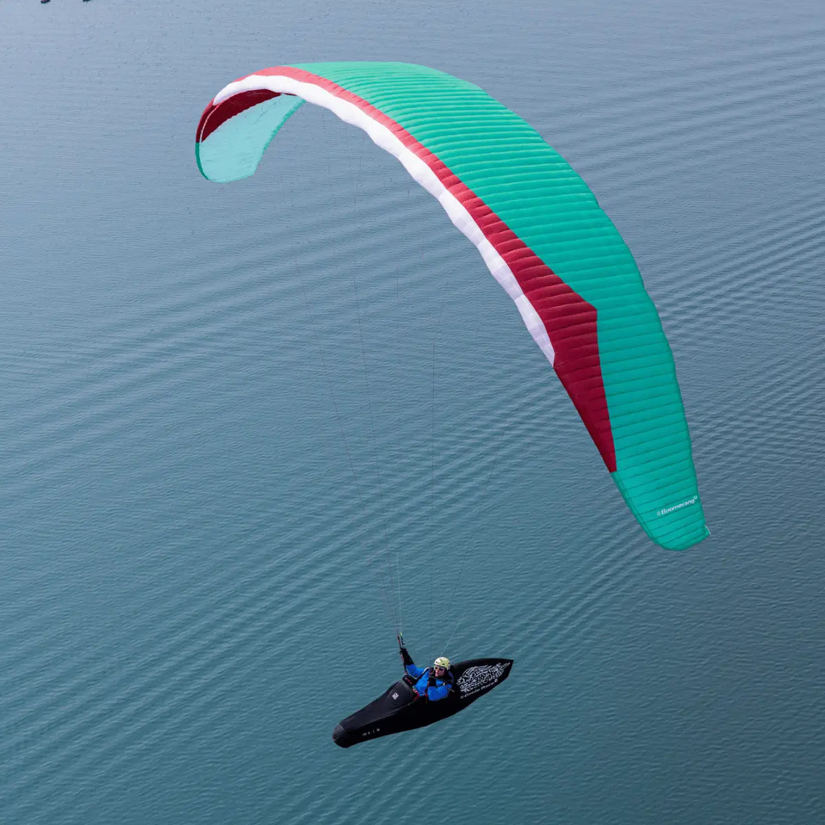 Gin Boomerang 12 EN-CCC Hochleistungswettkampf-Gleitschirm über Wasser, Pilot lenkt präzise unter zweifarbigem Flügel, ideal für erfahrene XC-Piloten.