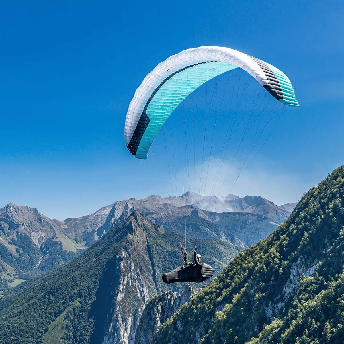 GIN Explorer 3 (High EN-B) Gleitschirm in Weiß und Türkis fliegt über einer Berglandschaft.