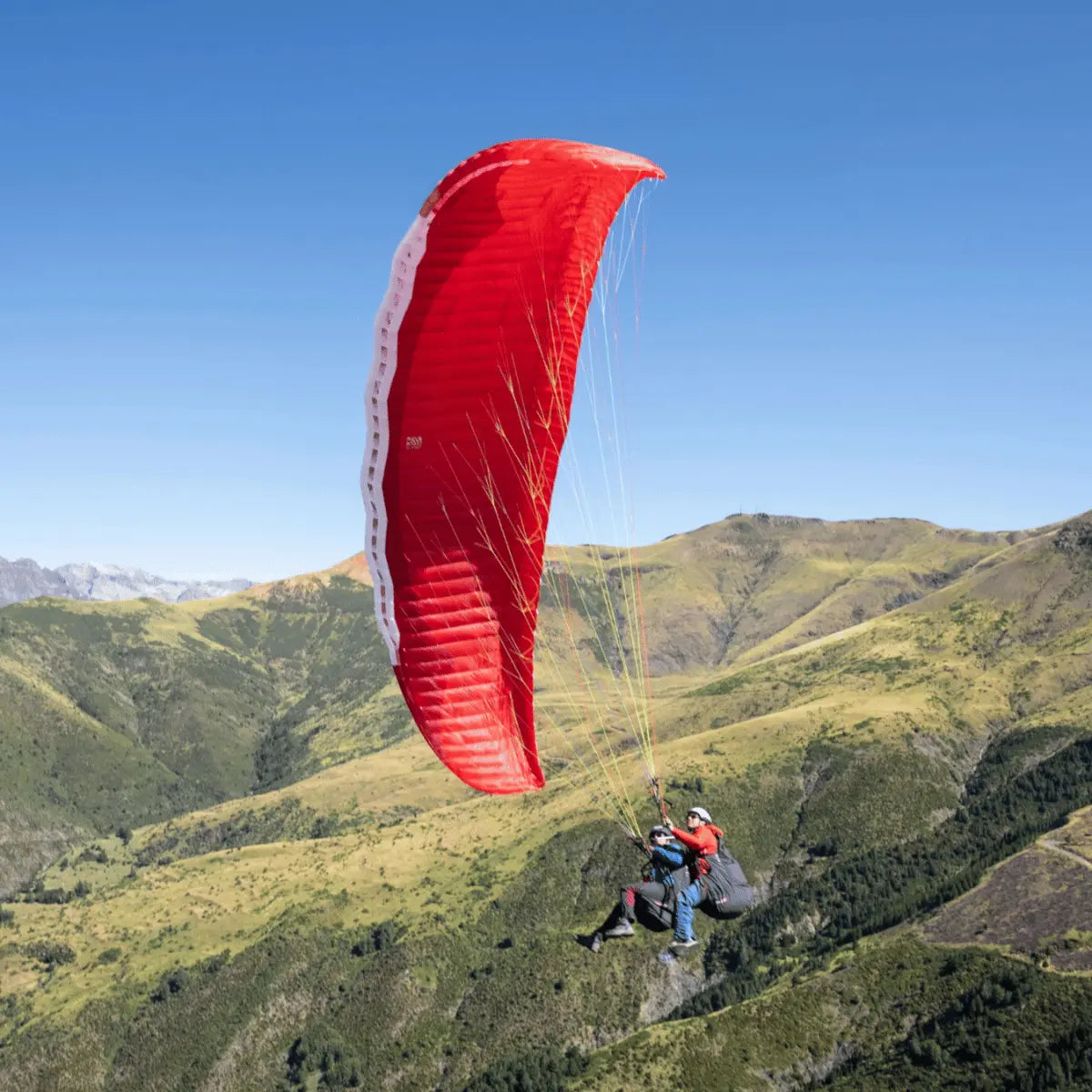 Zwei Personen fliegen mit dem Gin Fuse 4 Tandem EN-B Gleitschirm über grüne Hügel unter blauem Himmel. Ideal für professionelle und gewerbliche Nutzung.