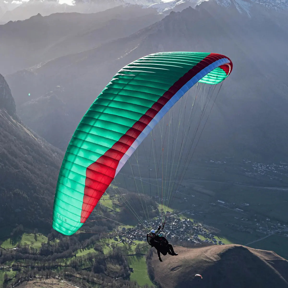 Ein Tandempilot fliegt mit dem Gin Fuse 4 Tandem EN-B Gleitschirm über eine malerische Berglandschaft, ideal für professionelle Anwendungen.