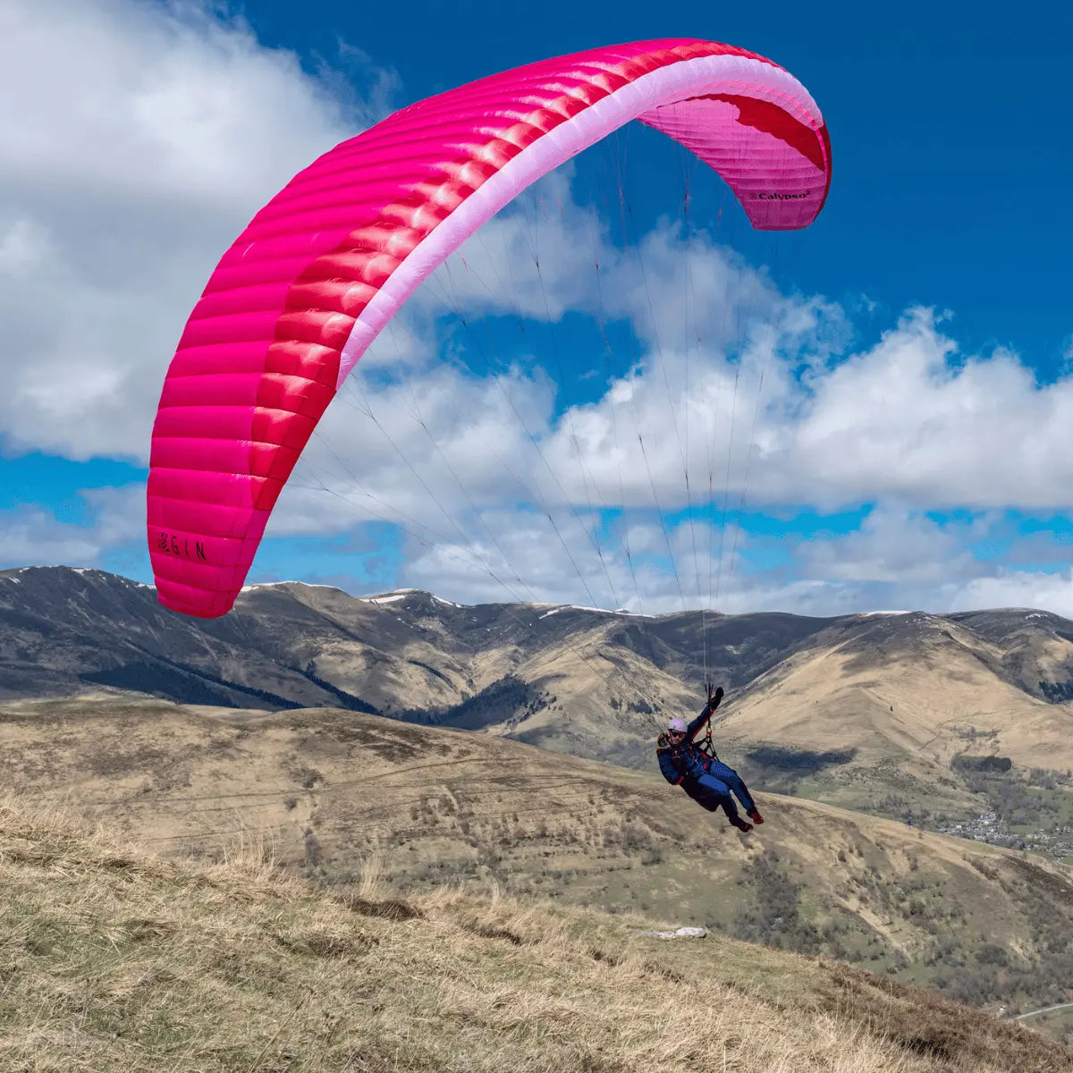 Gin Calypso 2 Light (Low EN-B) Gleitschirm, Pilot fliegt über trockenen Hügeln. Perfekt für Thermik und Hike & Fly, bietet kontrollierbares Handling und Stabilität.