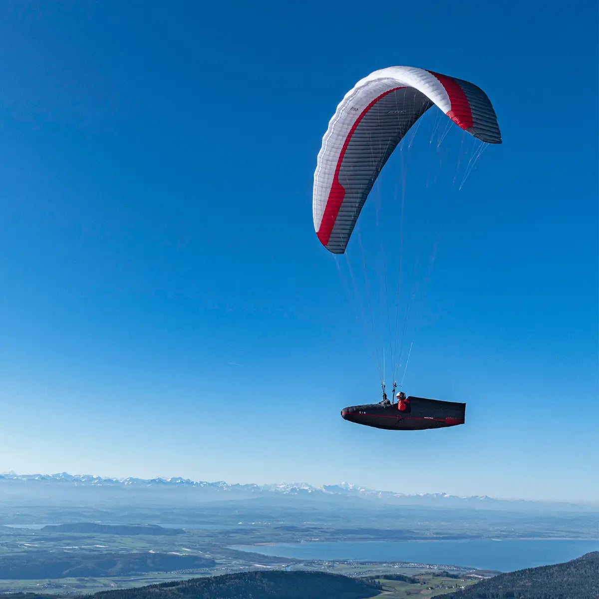 Gin GTO 3 (EN-C) Gleitschirm fliegt über Landschaft; Pilot in Hängegurt. Höchstleistung für erfahrene XC-Piloten, ideal für lange Streckenflüge.