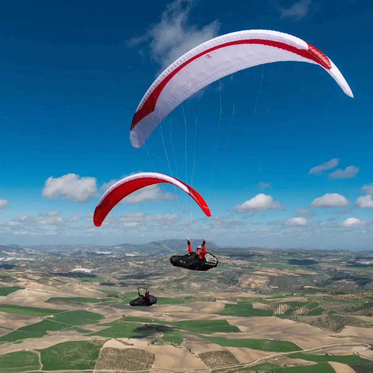 Gin Leopard (EN-D) - Competition Gleitschirm: Zwei Piloten unter rot-weißen Schirmen über landwirtschaftlichen Feldern, ideal für erfahrene XC- und Wettbewerbsflieger.