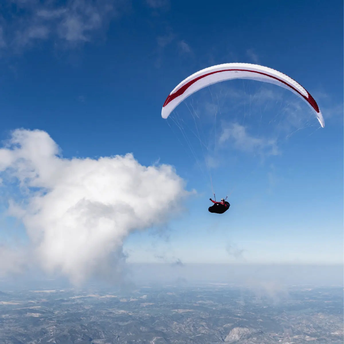 Person gleitet hoch am Himmel mit einem Gin Leopard (EN-D) Wettkampf-Gleitschirm, rotes und weißes Segel, ideal für erfahrene XC-Piloten.