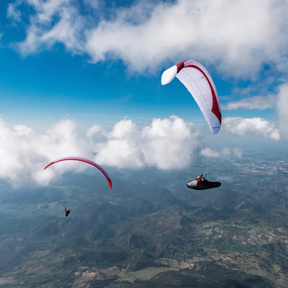 Zwei Gleitschirmpiloten mit Gin Leopard (EN-D) - Competition fliegen hoch über einer hügeligen Landschaft, ideal für erfahrene XC- und Wettkampf-Piloten.