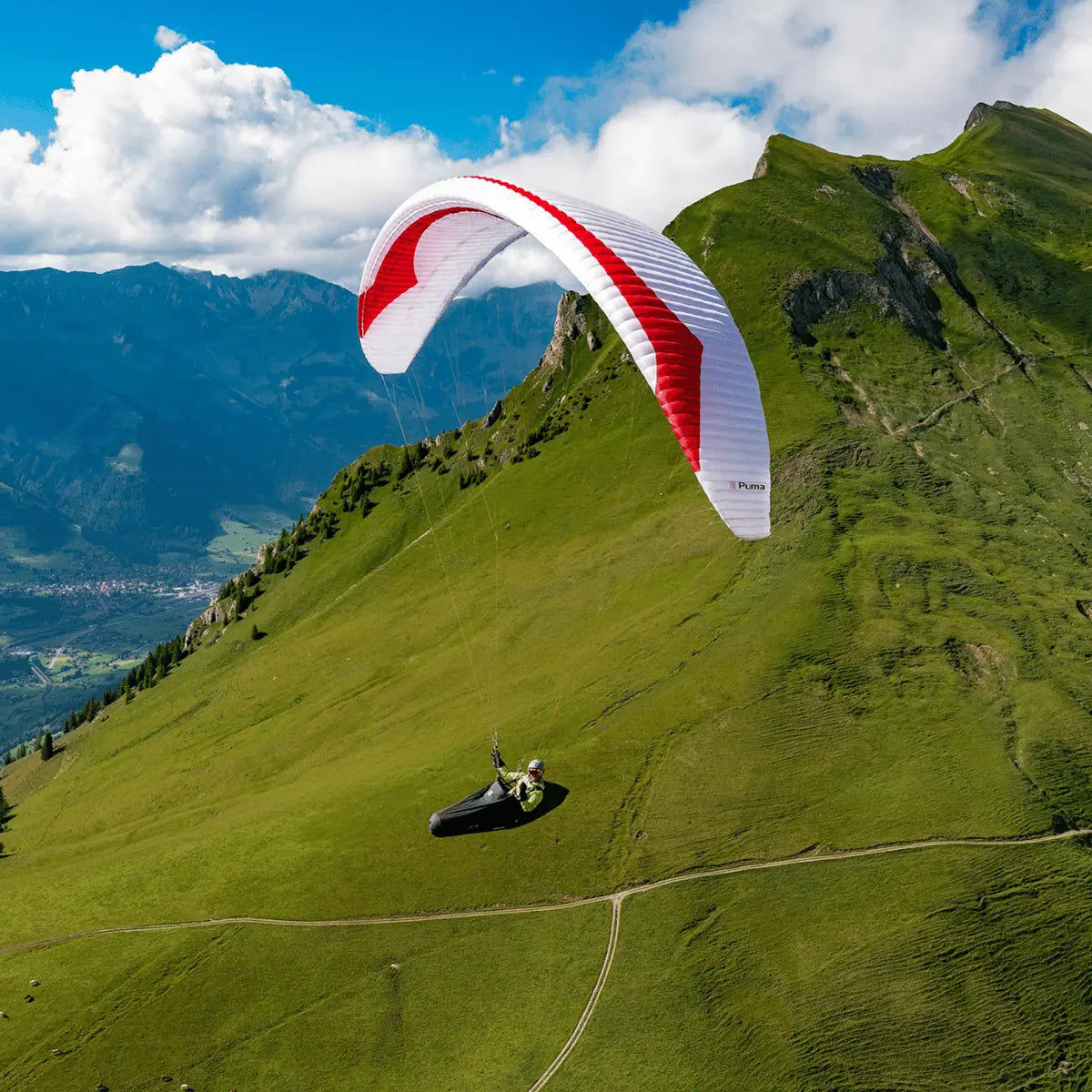 Gin Puma Light (EN-D) Paraglider über grüner Berglandschaft, ideal für erfahrene Wettkampfpiloten, bietet maximale Leistung bei reduziertem Gewicht.
