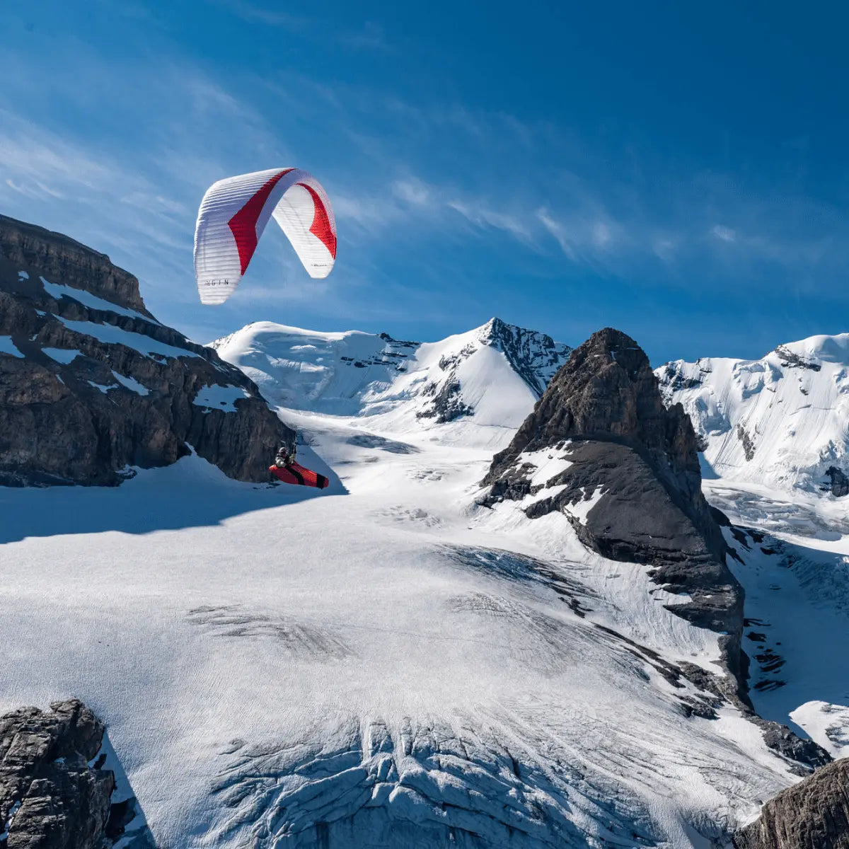 Gin Puma Light (EN-D) - Competition: Ein weiß-roter Paragleiter schwebt über schneebedeckten Alpengipfeln, ideal für XC- und Wettkampfpiloten, bietet hohe Leistung bei geringem Gewicht.