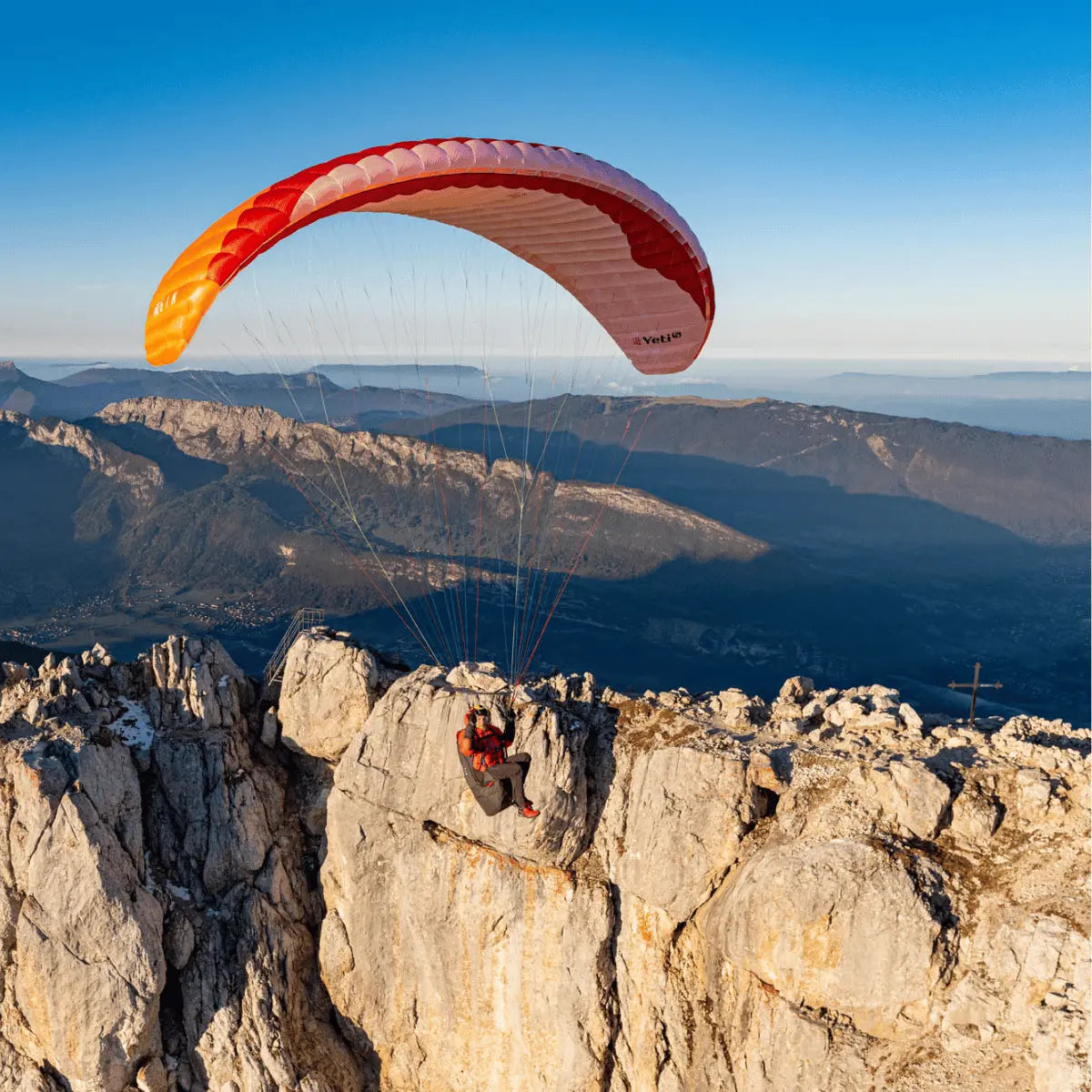 Alleinstehender Paraglider mit rotem Gin Yeti 6 Hike & Fly (EN-A) Schirm, bereit für sicheren Start von alpiner Klippe mit klarer Aussicht auf Berglandschaft.