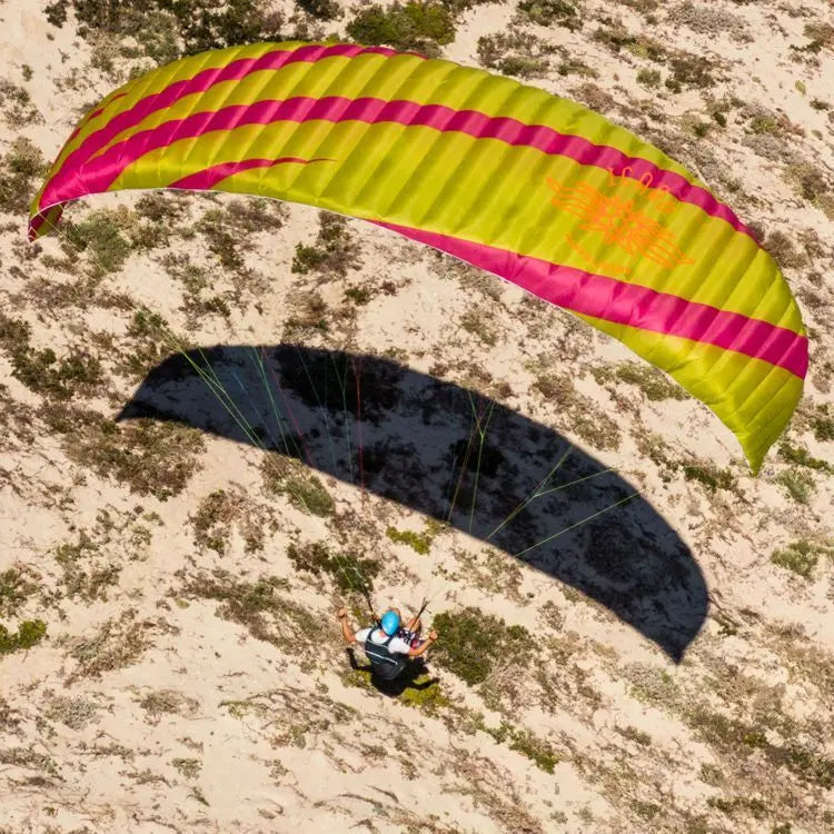 Icaro Pica 2 Gleitschirm im Flug über Sand, ideal für sichere und einfache Gleitschirmschulung und freies Fliegen, getragen von einem Helm tragenden Piloten.