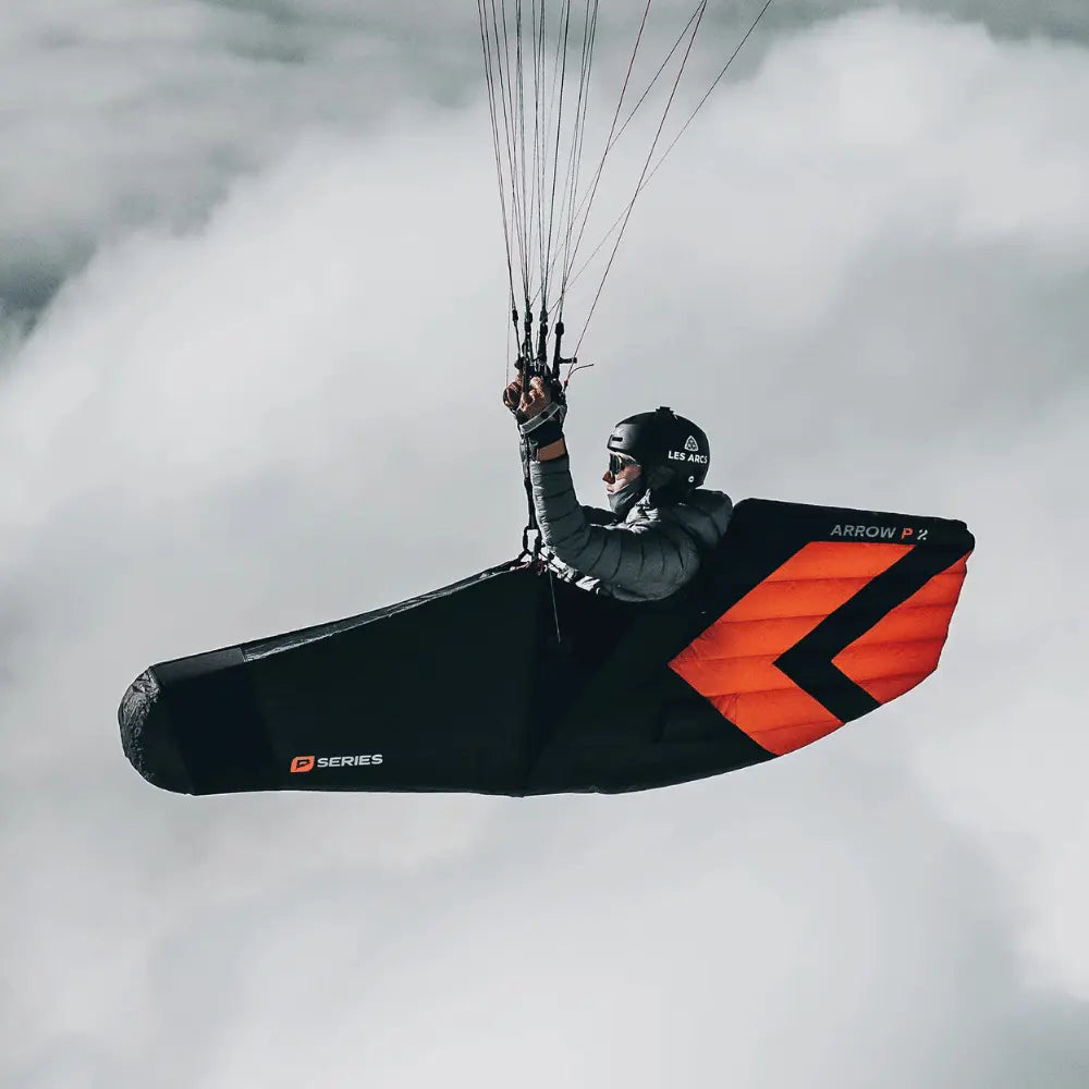 Person fliegt mit Niviuk Arrow P 2 Ultraleicht Liegegurtzeug, perfektioniert für Aerodynamik und Komfort, unter einem Gleitschirm, in einer ergonomischen Sitzposition über den Wolken.