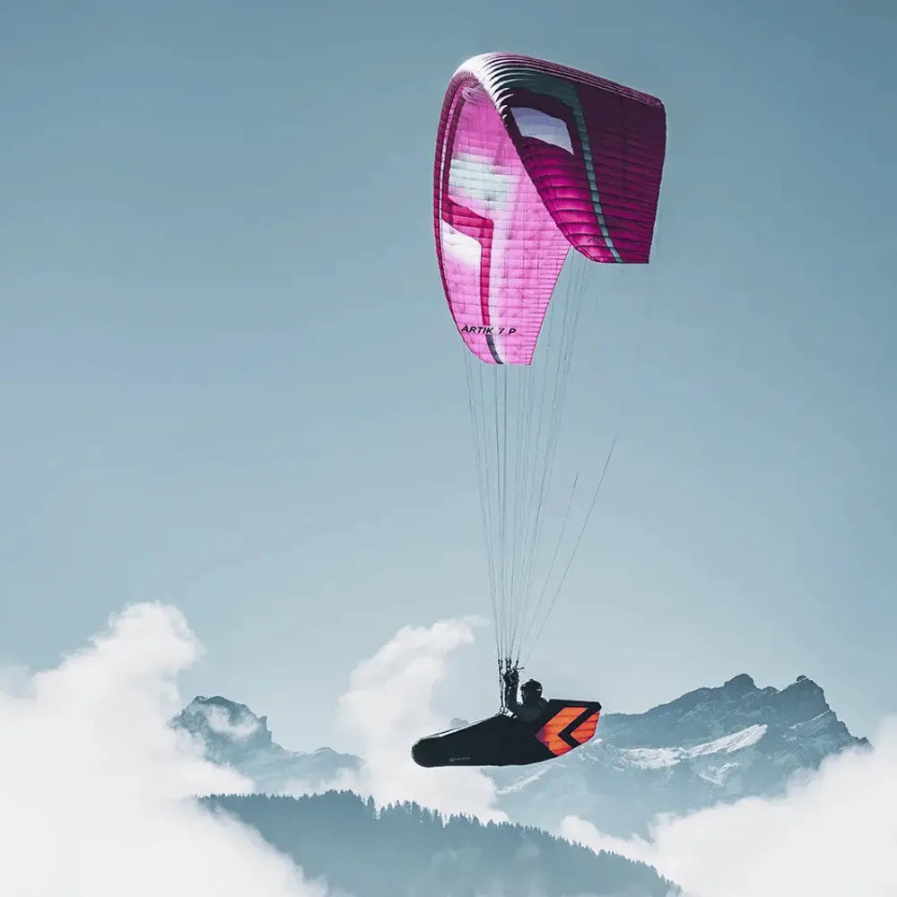Gleitschirmflieger über Bergkamm mit Niviuk Arrow P 2 Liegegurtzeug, optimiert für aerodynamisches Fliegen und Komfort, unter einem pinken ARTIK 7 P Schirm.