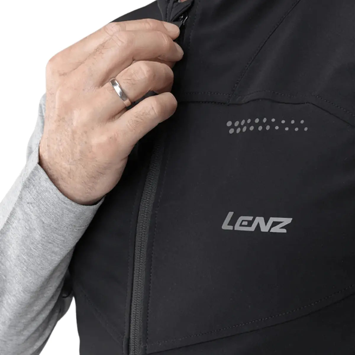 Schwarze Lenz HEAT Weste mit reflektierenden Details und Reißverschluss, getragen von einer Person mit einem Silberring.