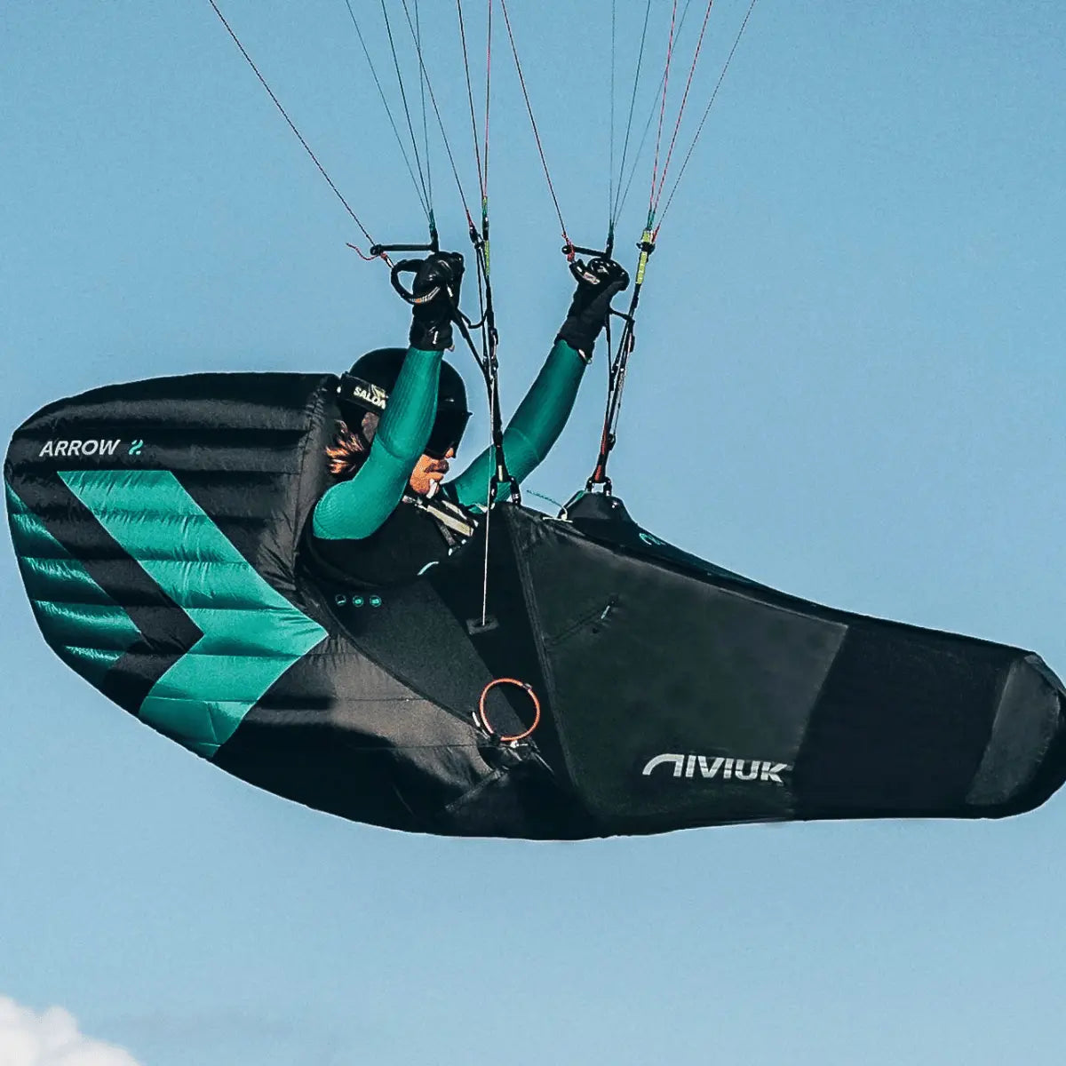 Niviuk Arrow 2 Liegegurtzeug in Schwarz und Türkis mit aerodynamischer Form, ideal für XC- und Wettkampfpiloten, zeigt den Piloten im Flug.