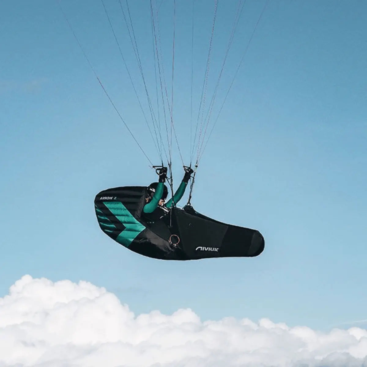 Niviuk Arrow 2 Liegegurtzeug in Schwarz-Türkis beim Gleitschirmfliegen mit Blick auf Wolken.