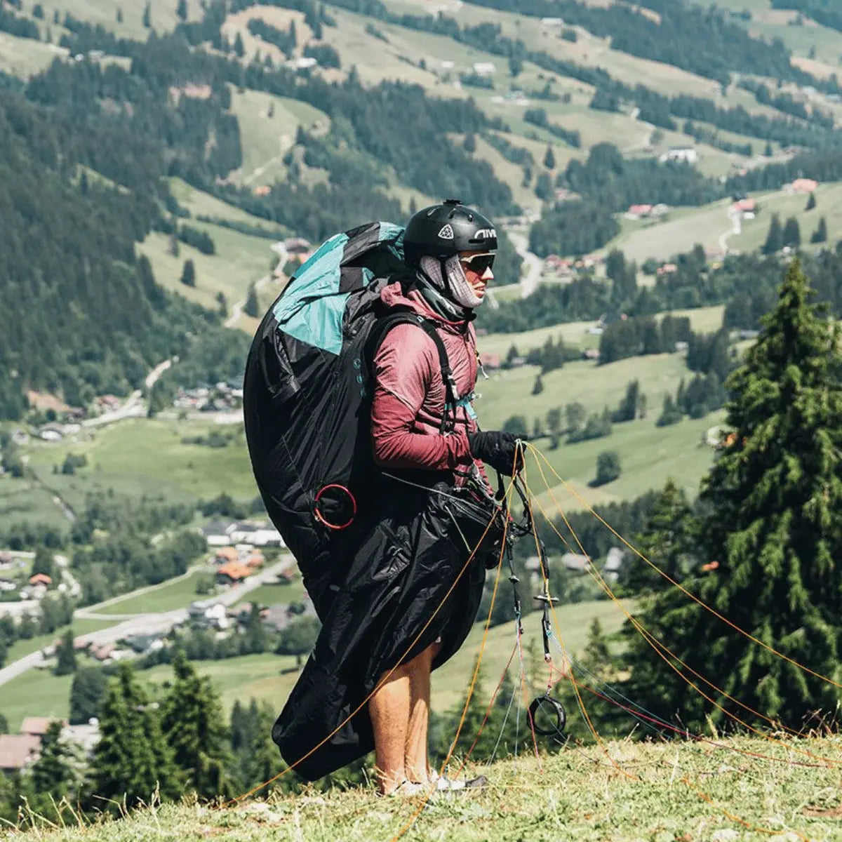 Ein Pilot in einem Niviuk Arrow 2 Liegegurtzeug mit Helm und Gleitschirm, bereit zum Start in einer malerischen Berglandschaft.