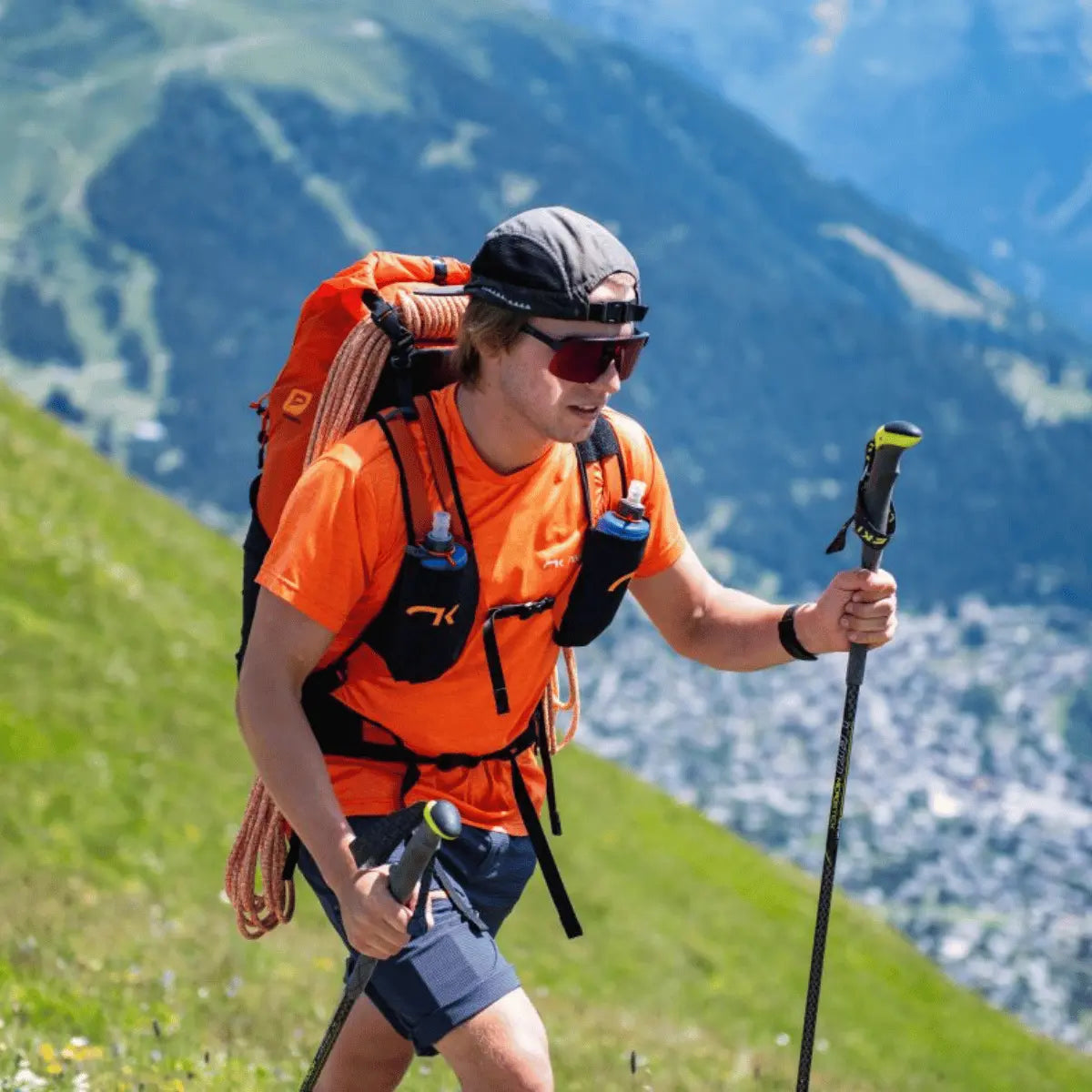 Ein Mann mit einem orangefarbenen Niviuk Expe Rucksack und Wanderstöcken wandert auf einem bergigen Hang.