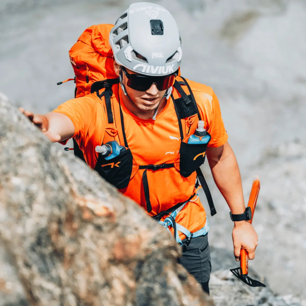 Bergsteiger mit orangefarbenem Niviuk Expe Rucksack und Helm klettert auf felsigem Terrain mit Eispickel.