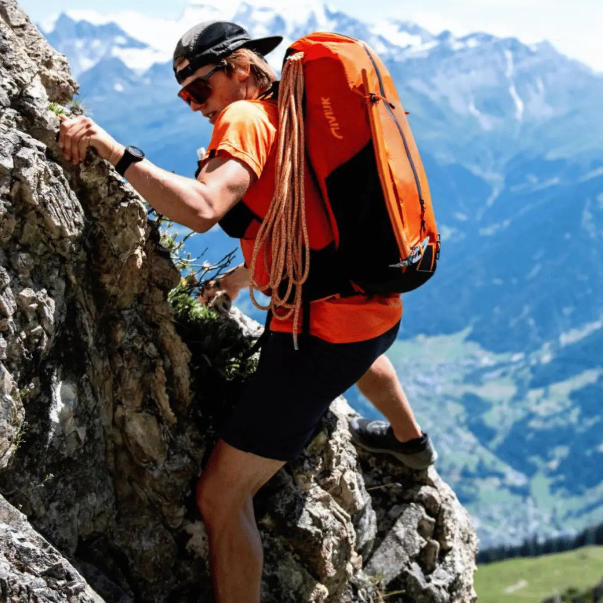 Mann beim Klettern in den Alpen mit einem orangefarbenen Rucksack mit hoher Bequemlichkeit, der auf dem Rücken getragen wird.